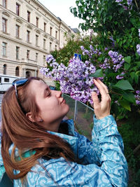 Pretty young woman with brown hair sniffing lilac flowers blooming in spring, beauty, magic scent