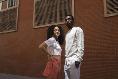 Woman with hand on hip standing with male friend in front of wall