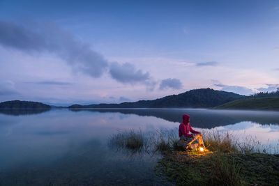 Rear view of woman standing by lake against sky during sunset