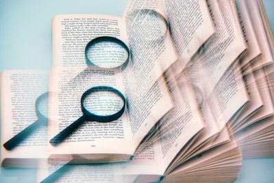 Digital composite image of magnifying glass and book on blue background