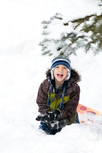 Portrait of cute boy sitting on snow covered land