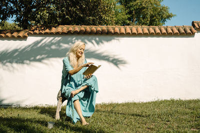 Woman reading book while sitting at backyard on sunny day