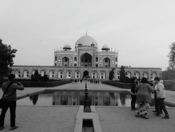 People at humayun's tomb, unesco world heritage site against clear sky and in front of still water