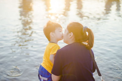 Rear view of mother kissing son against lake during sunset