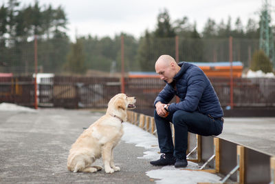 Rear view of man with dog sitting outdoors