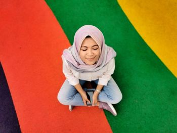 High angle view of woman with eyes closed wearing hijab while sitting on colored floor