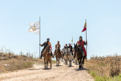 People riding horses on field against sky