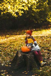 A little girl and a boy children are sitting on a tree stump with a large pumpkin in an autumn park