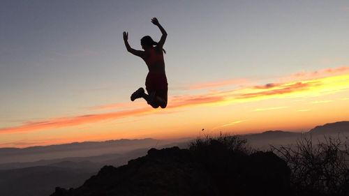 Silhouette woman jumping over mountain against sky during sunset