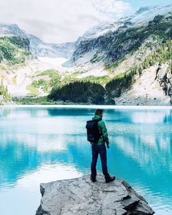 Rear view of man standing on snow covered mountain lake