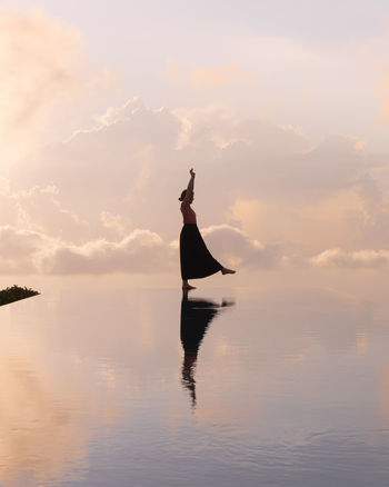 MAN WITH ARMS RAISED IN SEA AGAINST SUNSET SKY