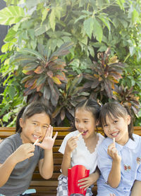 Cheerful female friends eating french fries on bench at public park