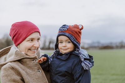 Portrait of smiling woman carrying baby girl in park during winter
