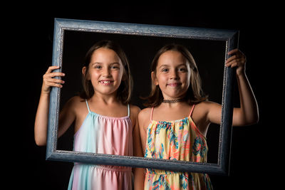 Portrait of girl with sister holding frame against black background