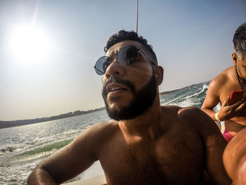 Portrait of shirtless man at beach against sky on sunny day