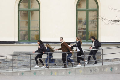Cheerful teenage girls and boys running on walkway of high school