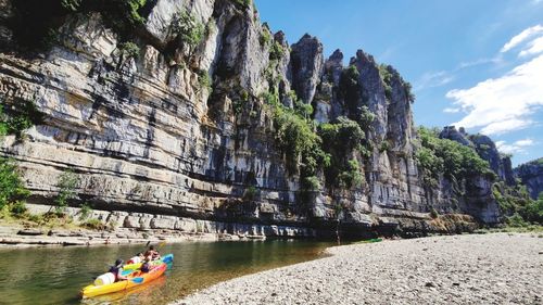 People on rock by mountain against sky