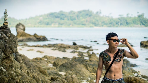 Shirtless man wearing sunglasses while standing at beach