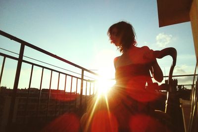 Woman standing by railing against sky during sunset