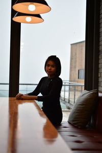 Portrait of young woman sitting on sofa by table against window in cafe