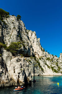 Scenic view of mountain by sea against clear blue sky