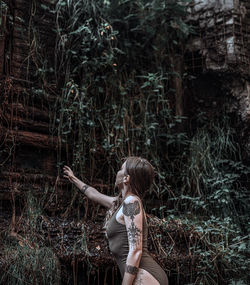 Side view of woman standing by tree in forest