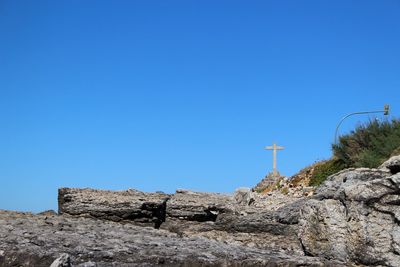 Low angle view of cross on rock against clear blue sky