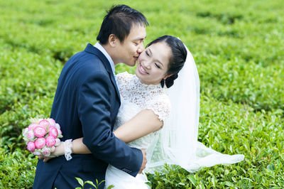 Bridegroom kissing bride amidst plants on field