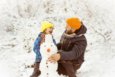 Joyful dad and son enjoying building a snowman.