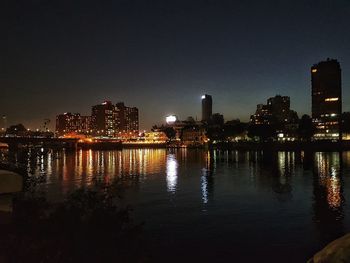 Illuminated buildings by river against sky at night