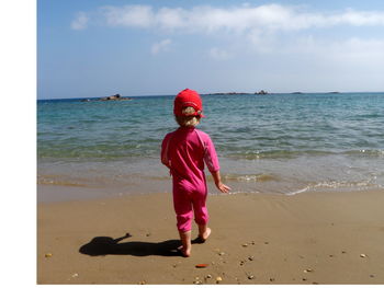 Rear view of child walking towards sea shore against sky