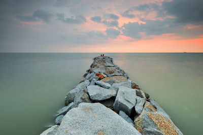 Groynes by sea against cloudy sky during sunset