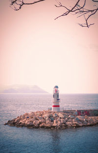 Lighthouse by sea against clear sky