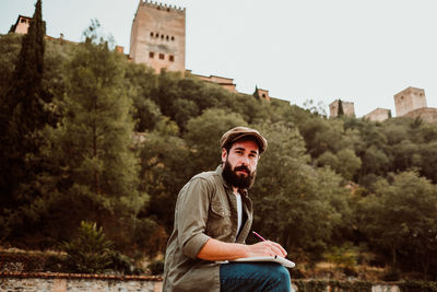 Portrait of man writing in book while sitting outdoors