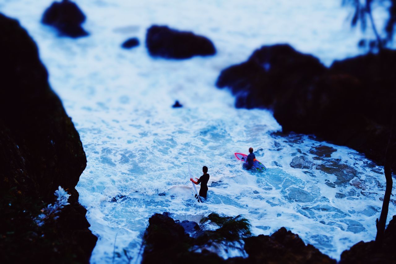 HIGH ANGLE VIEW OF PEOPLE ON ROCKS AT SHORE