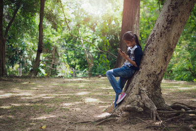 Young girl using mobile phone under big tree in the garden under sunlight.