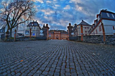 Cobblestone street amidst buildings against sky at sunset