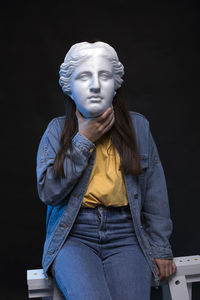 Young woman with aphrodite plaster mask wearing jeans