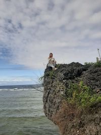 Man on rock by sea against sky