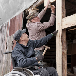 Happy elderly man  in a wheelchair iworking and building something in his yard. a friend helps him.