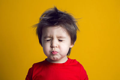 Cheerful baby boy in red t-shirt stands on yellow background