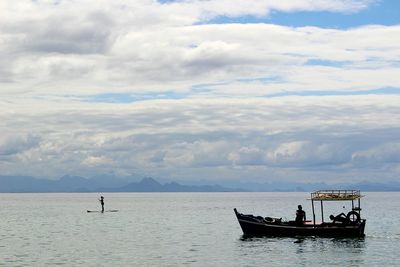 Woman paddleboarding while men in boat against cloudy sky on river