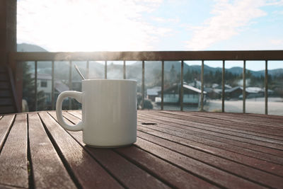 Coffee cup on table by window against sky