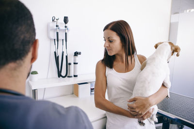 Woman carrying dog talking with veterinarian in hospital