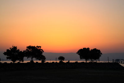 Silhouette trees on landscape against orange sky