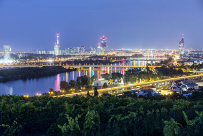 Illuminated buildings by river against sky in city at night