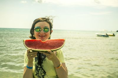 Portrait of smiling woman holding watermelon slice against sea during summer