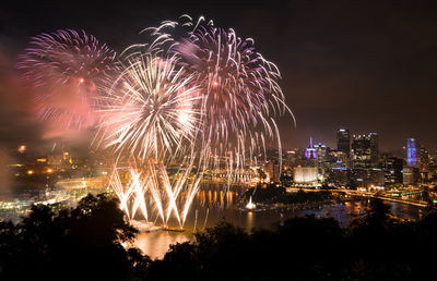 Firework display over illuminated city against sky at night