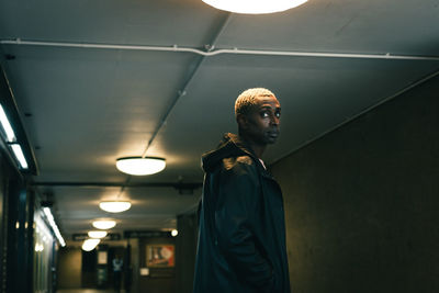 Side view of adult black guy in outerwear looking away while standing in dark underground passage in city