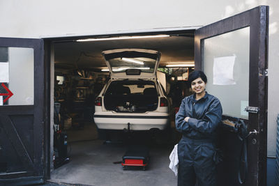 Portrait of confident female mechanic standing with arms crossed at entrance of auto repair shop